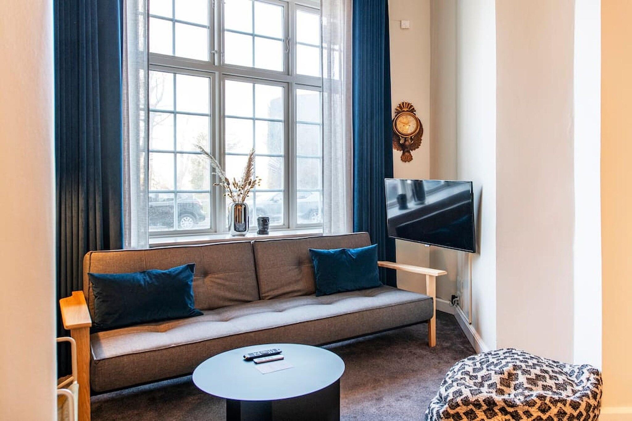 A living room with a sofa, a coffee table, a flat-screen TV, and a window with curtains.