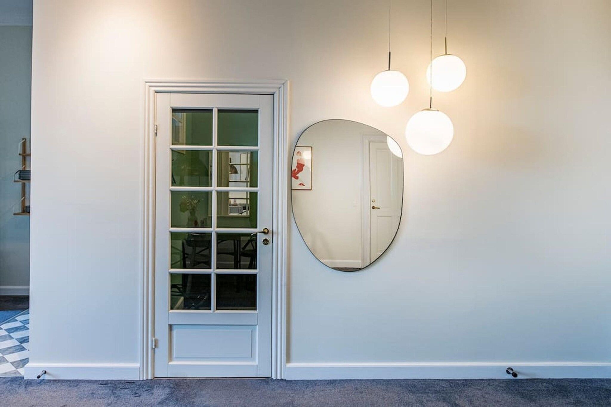 A hallway with a white door, a round mirror, and three hanging lights.