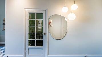A hallway with a white door, a round mirror, and three hanging lights.