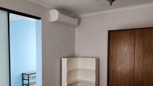 Un dormitorio con cama, armario en esquina, estante empotrado, ventilador de techo y aire acondicionado.