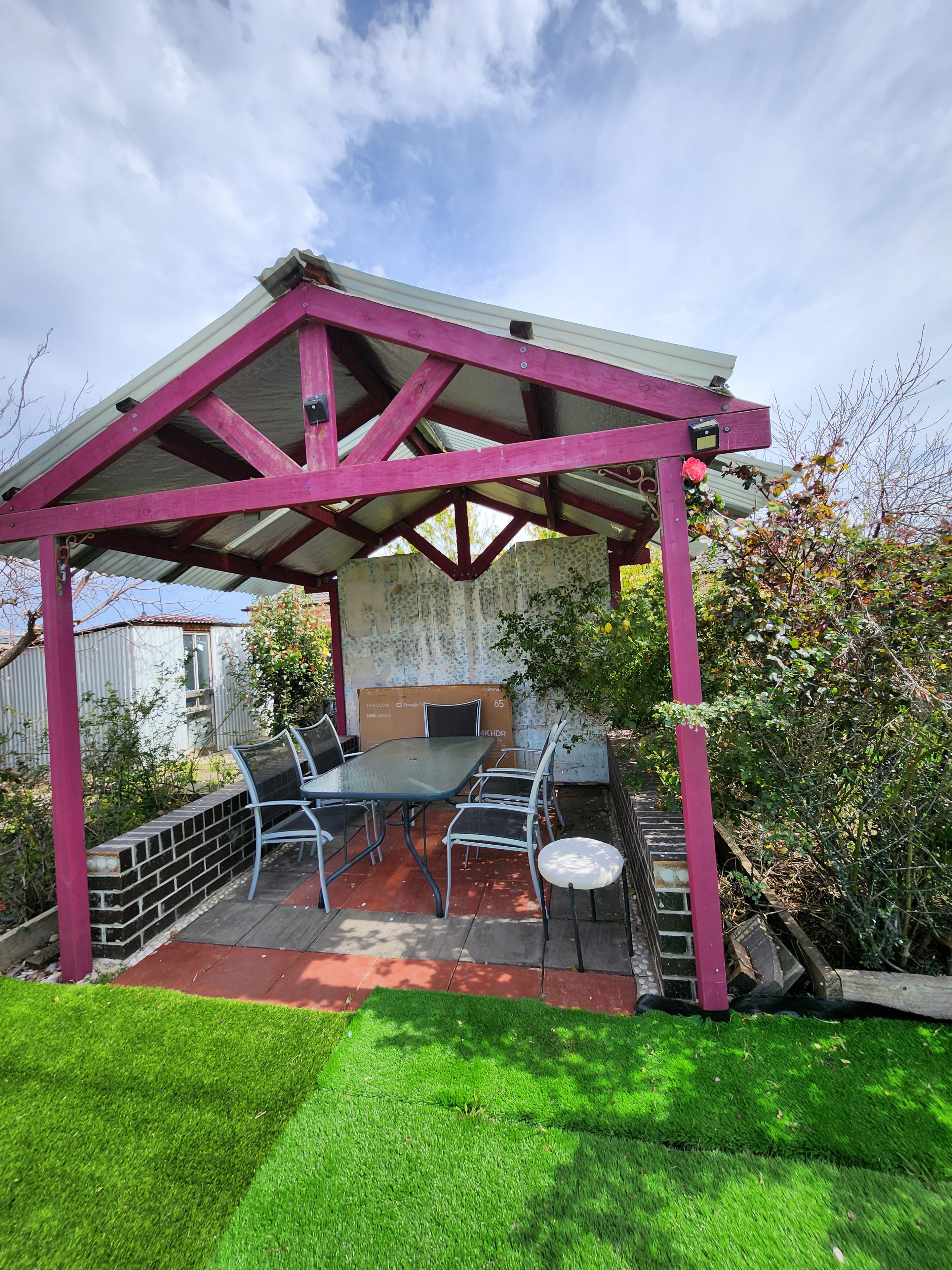 A covered patio with a table and chairs, surrounded by a brick wall and greenery.