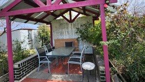 Un patio techado con una mesa y sillas, rodeado por un muro de ladrillo y follaje.