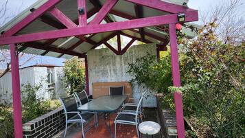 A covered patio with a table and chairs, surrounded by a brick wall and greenery.