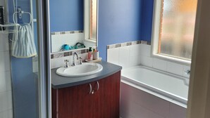 Un baño con cabina de ducha de vidrio, lavamanos, espejo, bañera y ventana.