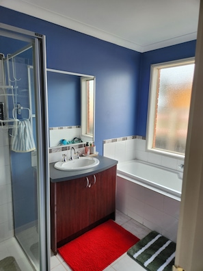 Ein Badezimmer mit Duschkabine aus Glas, Waschbecken, Spiegel, Badewanne und Fenster.