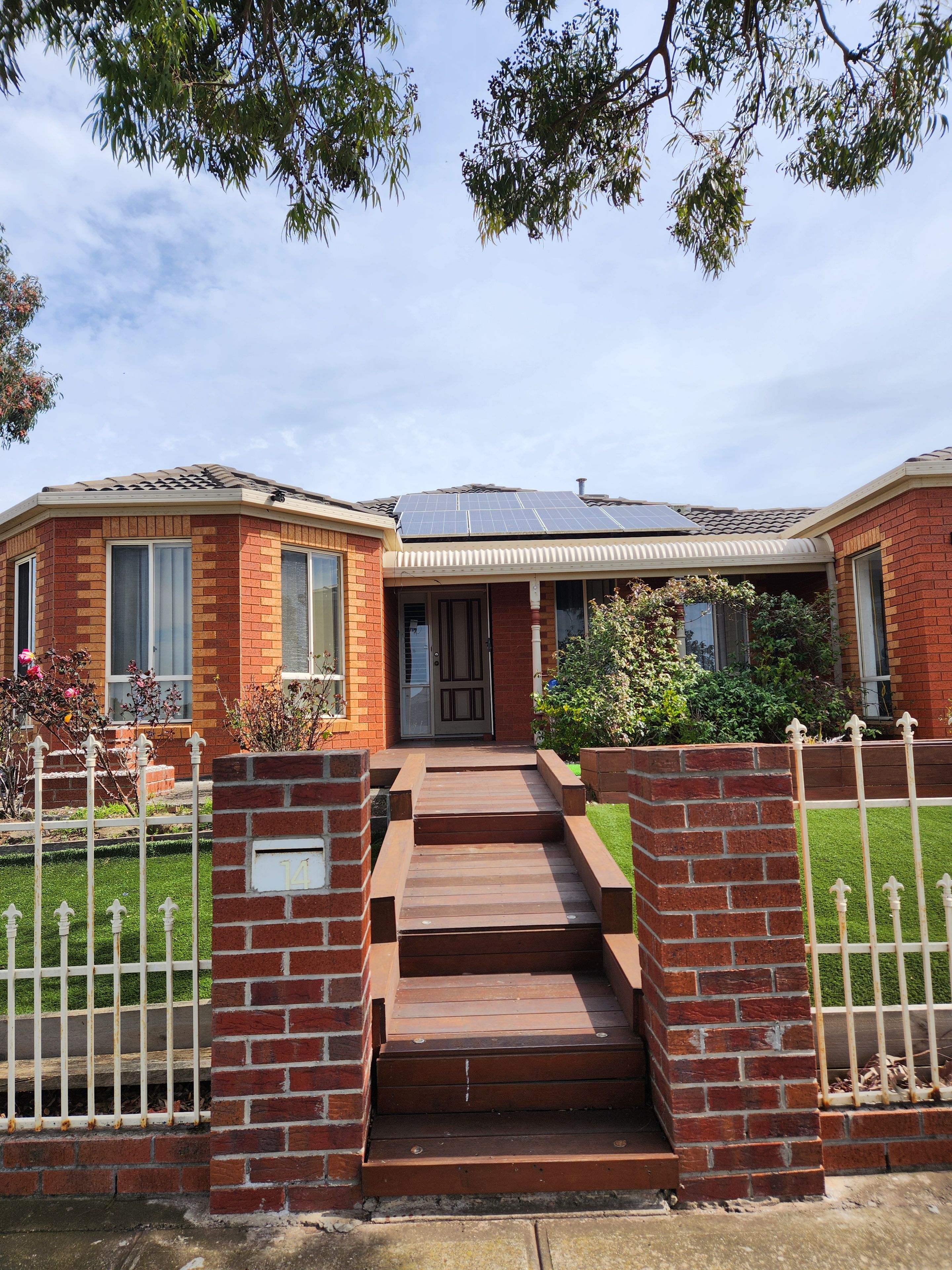 A two-story brick house with a solar panel roof, a front porch, and a gated entrance.