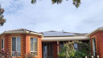 A two-story brick house with a solar panel roof, a front porch, and a gated entrance.