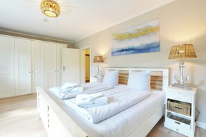 Ein Schlafzimmer mit einem großen Bett, weißer Bettwäsche, einem Gemälde an der Wand und zwei Nachttischlampen.