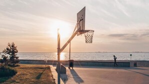 En utomhusbasketplan med en korg, en soptunna och en person som går på avstånd.