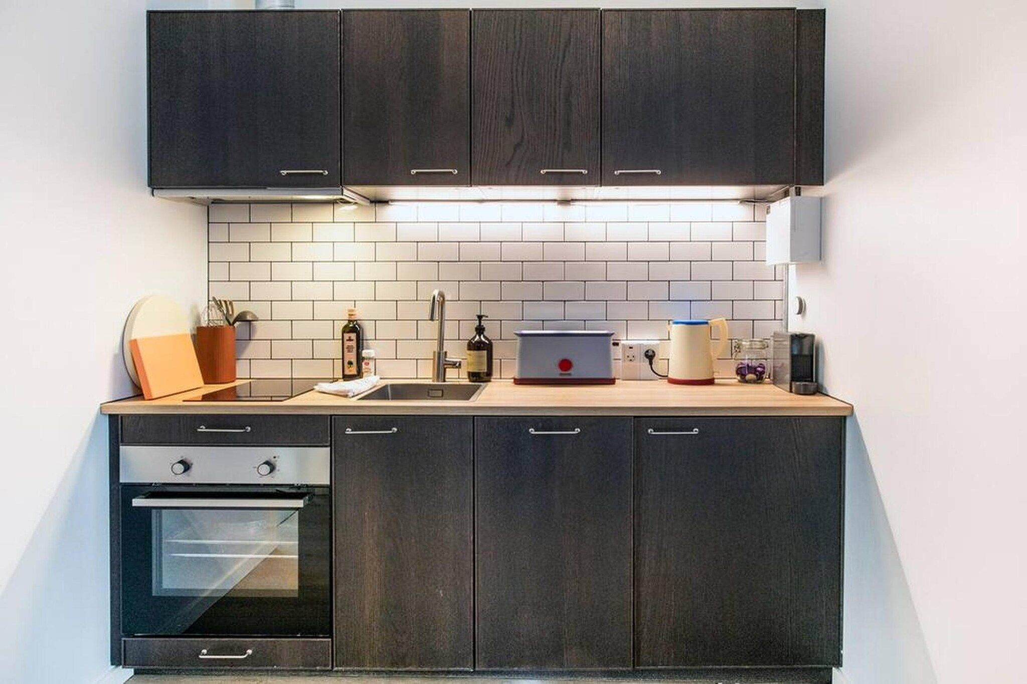 A modern kitchen with dark cabinetry, a white tiled backsplash, and a built-in oven.