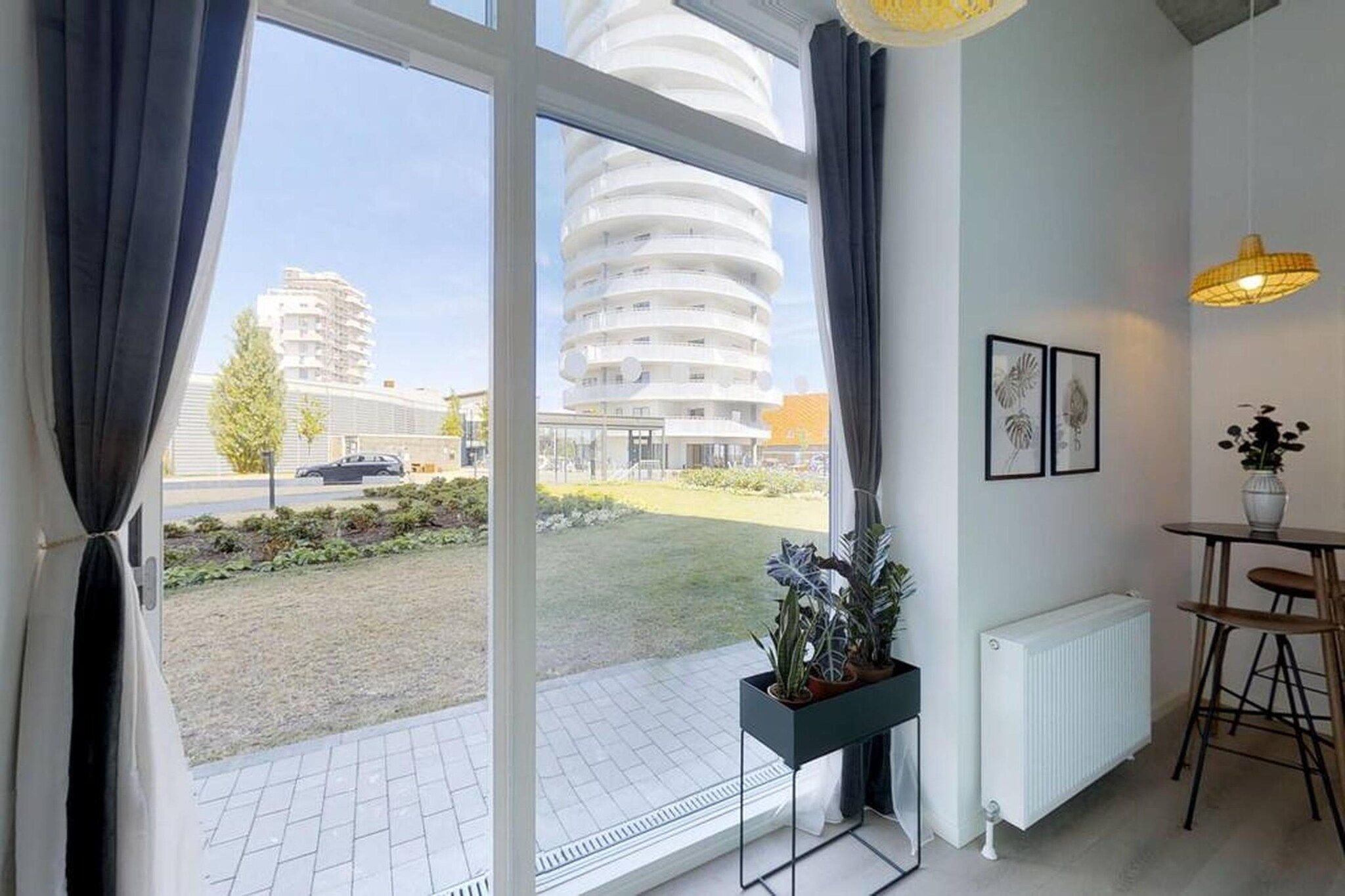 Ein modernes Interieur mit großen Fenstern, einem Heizkörper, einem kleinen Tisch und einer Topfpflanze.