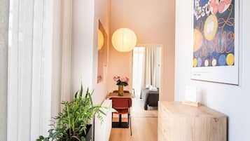 Un intérieur moderne avec un comptoir d’accueil en bois, un coin repas avec une chaise rouge et un couloir menant à une chambre.