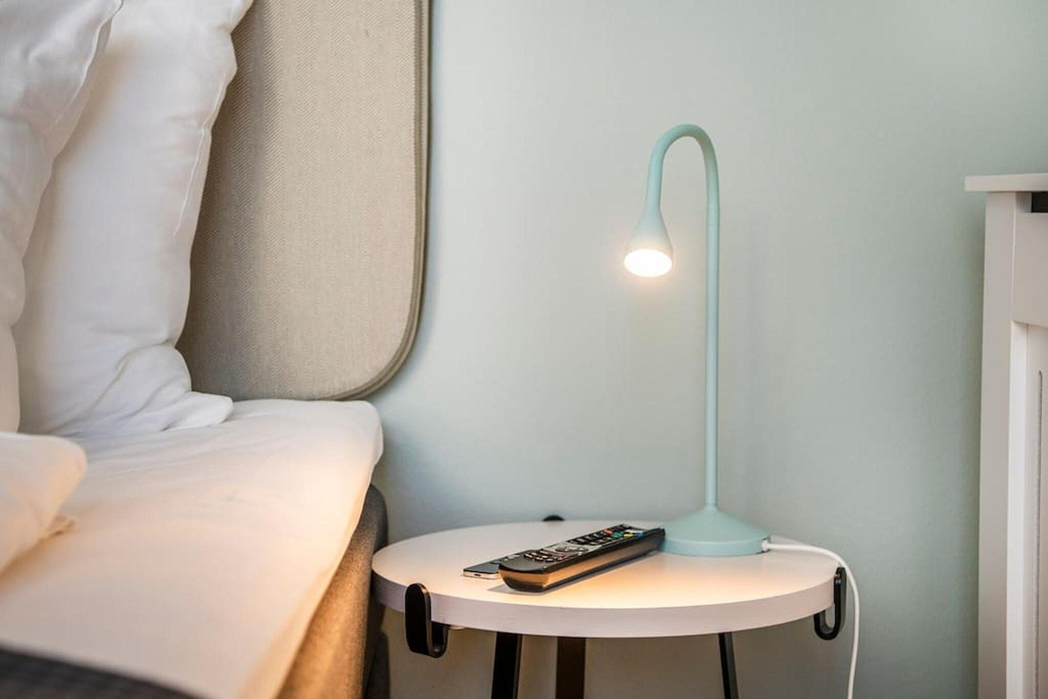 Ein Bett mit weißer Bettwäsche, ein Nachttisch mit Fernbedienung und eine moderne Stehlampe.