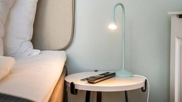 Ein Bett mit weißer Bettwäsche, ein Nachttisch mit Fernbedienung und eine moderne Stehlampe.