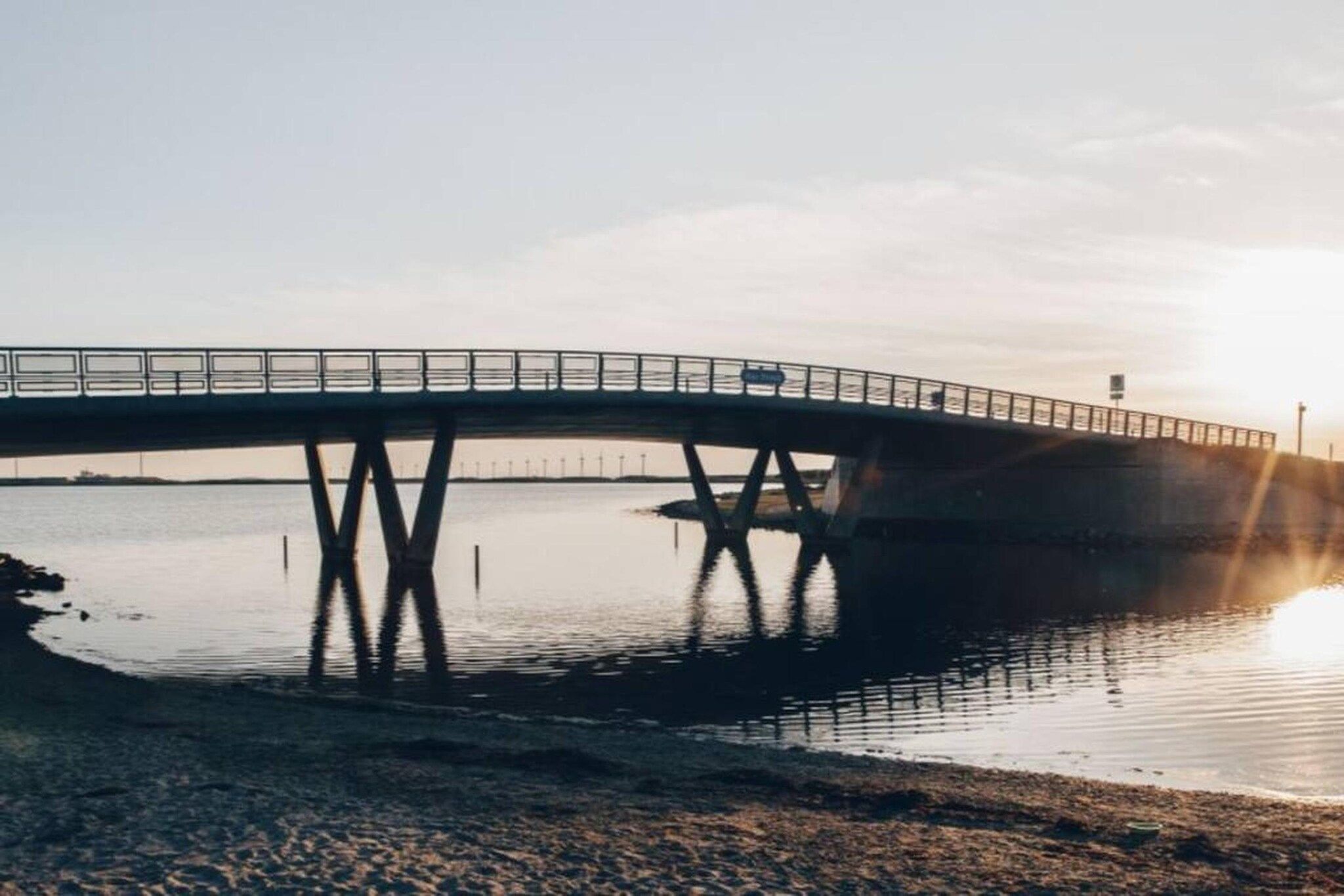 Een brug over stil water met een heldere lucht.