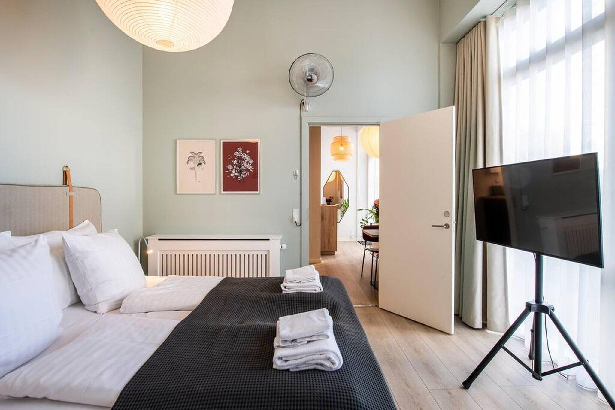 A hotel room with a bed, a TV on a stand, a radiator, and artwork on the wall.