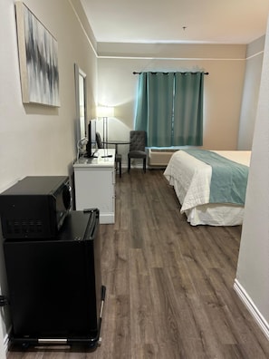 A compact hotel room with a bed, a desk with a chair, a small kitchenette, and a window with curtains. - La Quinta Inn Brownsville (Los Fresnos)