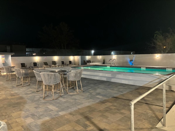 An outdoor pool area with lounge chairs and tables, surrounded by a low wall and a tiled floor. - La Quinta Inn Brownsville (Los Fresnos)