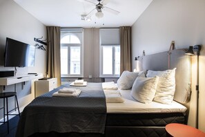Et hotelværelse med seng, natbord, fjernsyn og skrivebord.