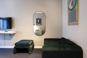 A room with a flat-screen TV, a round mirror, a green ottoman, a green sofa, and a colorful abstract painting on the wall. - Historic Center Copenhagen Home (København)
