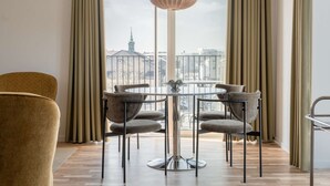 Un comedor moderno con una mesa redonda y cuatro sillas, una lámpara colgante y vistas de un paisaje urbano a través de grandes ventanales.