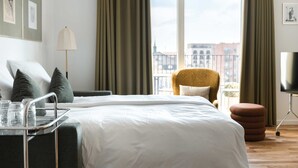 Habitación de hotel con cama, una silla, un mueble para televisión y ventana con cortinas.