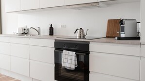 Una cocina moderna con armarios blancos, horno integrado, cafetera y tostadora.