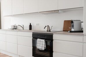 A modern kitchen with white cabinetry, a built-in oven, a coffee maker, and a toaster. - Coastal flat in Amager with balcony (København)