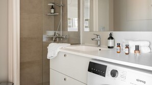 Un baño moderno con cabina de ducha de vidrio, lavabo blanco y lavavajillas empotrado.