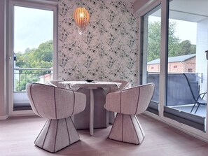 Ein Essbereich mit Tisch und Stühlen, einer Hängeleuchte und Blick durch große Fenster.