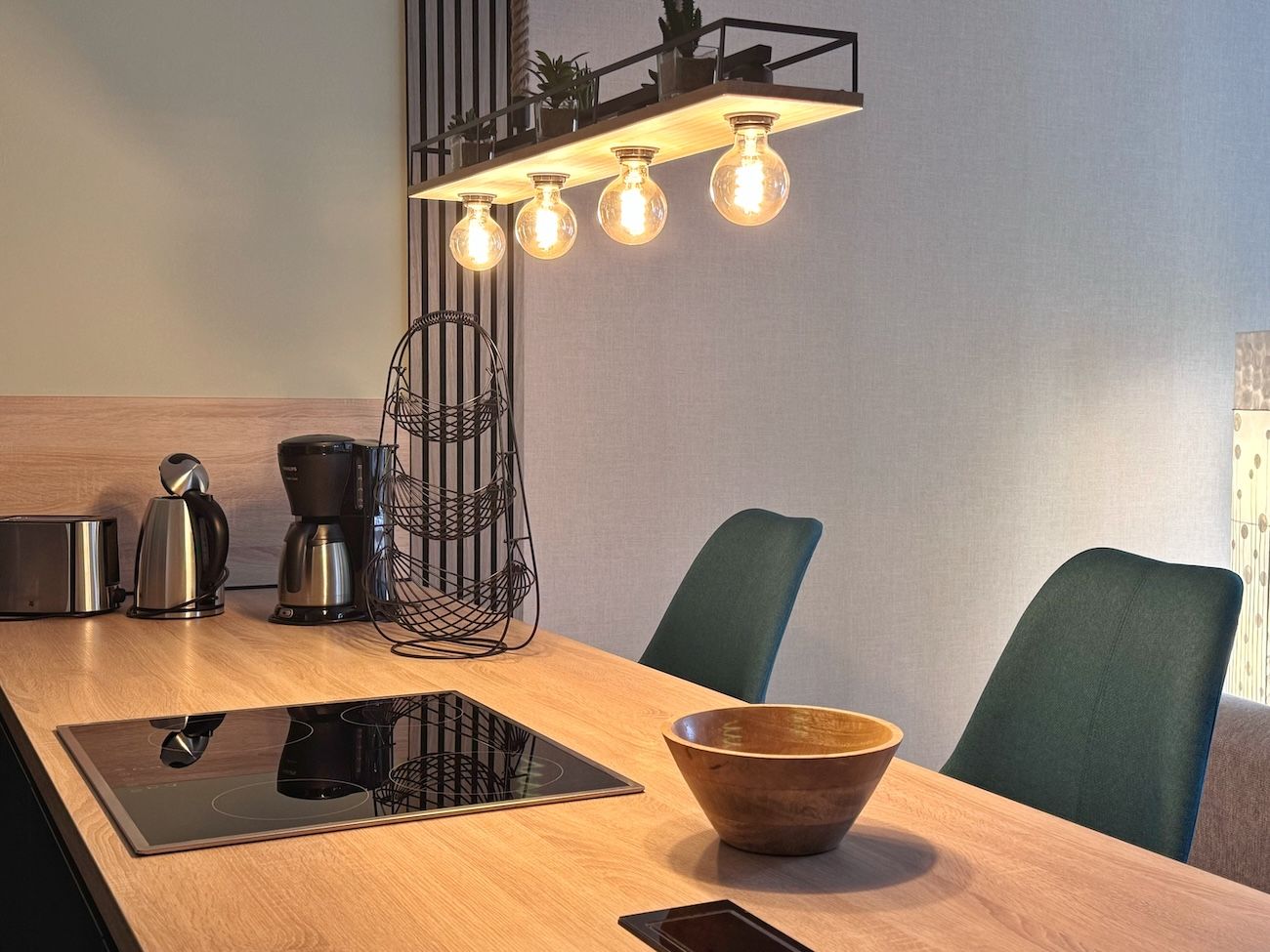 A modern kitchen with a wooden countertop, a built-in induction cooktop, a coffee maker, a toaster, and a hanging light fixture.