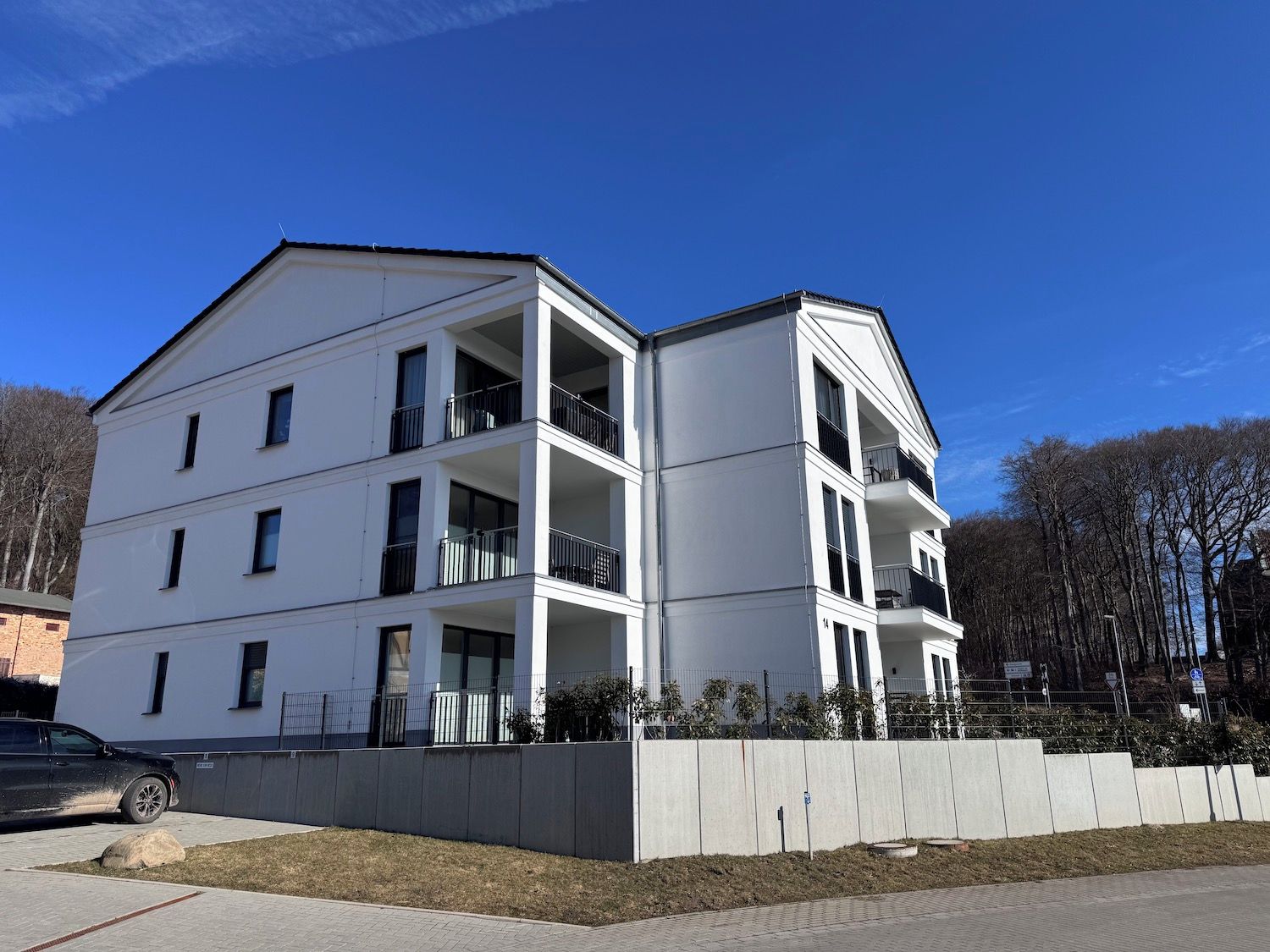 A multi-story building with balconies, a parking area, and a clear sky.