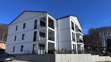 A multi-story building with balconies, a parking area, and a clear sky.