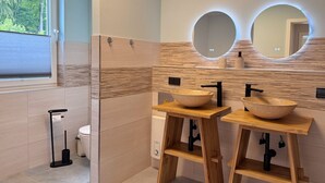 Uma casa de banho moderna com duas pias de vaidade em madeira, uma sanita e uma janela com estores.