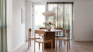 Un coin repas avec une table ronde, six chaises en bois, un vase de fleurs et une fenêtre avec des rideaux.