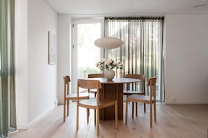 En matplats med ett runt bord, sex trästolar, en vas med blommor och ett fönster med gardiner.