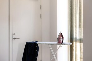 Habitació amb una porta blanca, una taula de planxar petita amb un ferro, i un teixit blau fosc penjat a la porta.