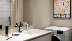 Une salle de bain avec un lavabo blanc, un miroir, des toilettes et un lave-linge.
