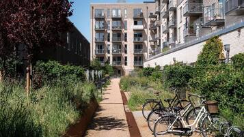 Un camino conduce a un moderno edificio de apartamentos con varios balcones y un aparcamiento para bicicletas.