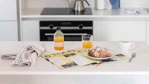 Une table de petit-déjeuner avec un journal, une bouteille de jus d’orange, un verre de jus d’orange, un croissant, une tasse de café et une fourchette.