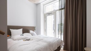 Une chambre à coucher avec un lit, des oreillers, une table de chevet et une fenêtre avec des rideaux.