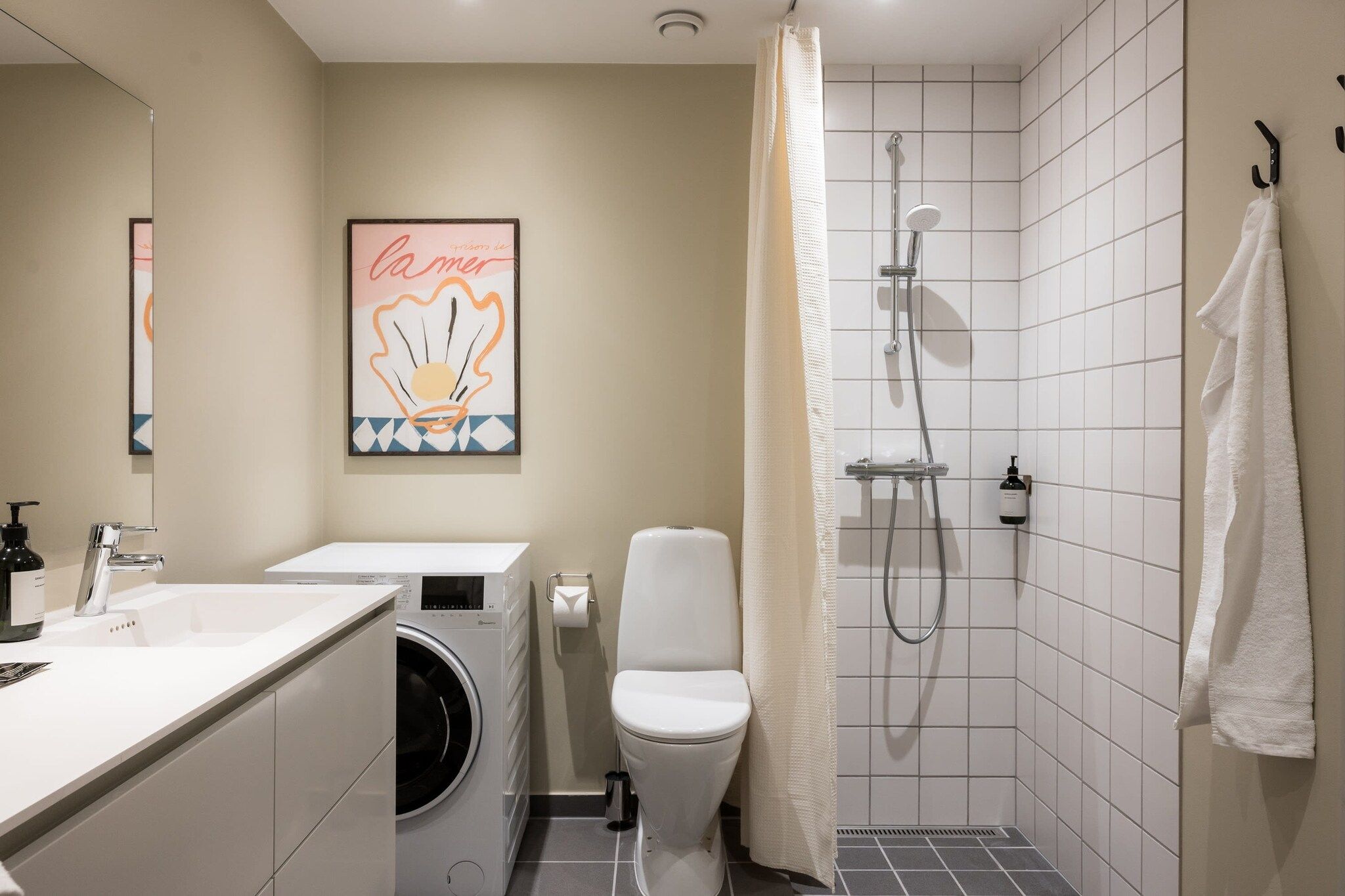 Un baño moderno con lavadora, inodoro, ducha y un perchero para toallas.