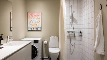 Un baño moderno con lavadora, inodoro, ducha y un perchero para toallas.