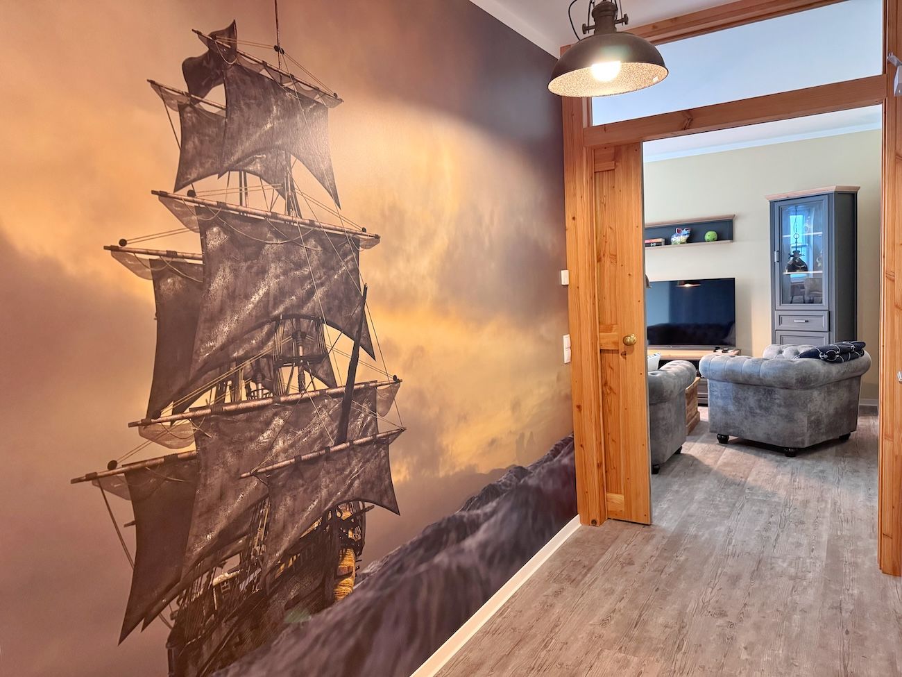Ein Zimmer mit einer großen Wandmalerei eines Schiffes, einer Holztür und einem grauen Sofa.