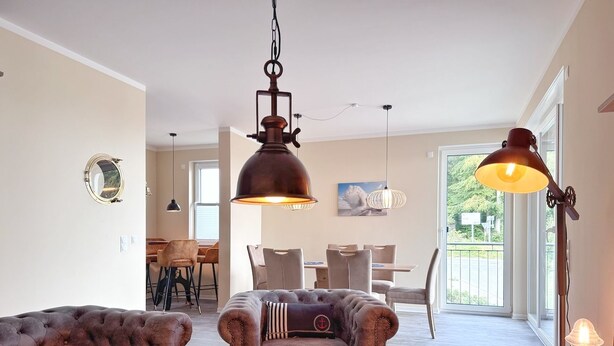 A living room with a sofa, armchair, and a coffee table with a decorative plate. There is a dining area with chairs and a table in the background. - Kogge 6 Apartment - Sassnitz (Sassnitz)