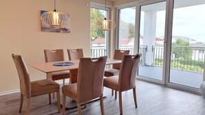 A dining area with a table and chairs, a pendant light, and a view through large windows. - Kogge 6 Apartment - Sassnitz (Sassnitz)