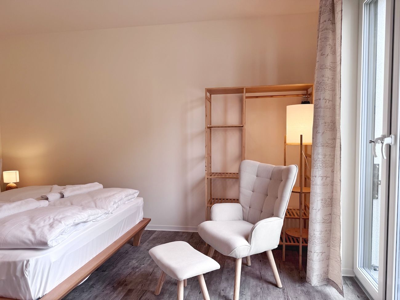 Ein Hotelzimmer mit Bett, Stuhl, Nachttisch und einem Fenster mit Vorhang.