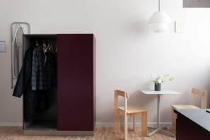A room with a wardrobe, a table, two chairs, a hanging light fixture, and a small vase with flowers. - Cozy Hideaway in Copenhagen (København)