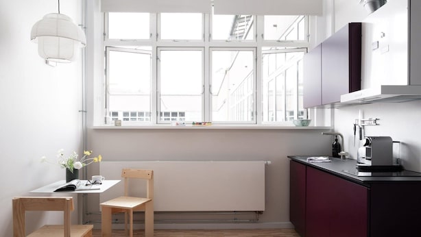 Une cuisine moderne avec une fenêtre, un radiateur, une chaise en bois, une table et une machine à café.