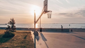 Un terrain de basket en plein air, avec un filet, un panier de basket et une personne qui marche au loin.